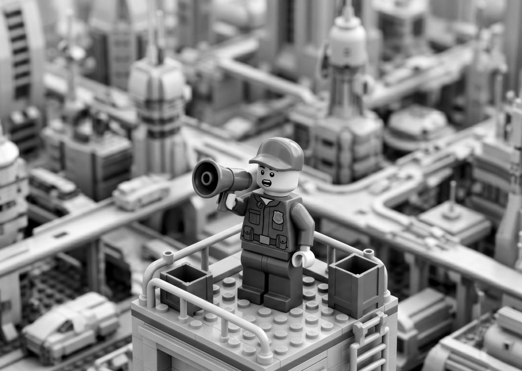 Black and white Lego character holding a megaphone on a futuristic city rooftop, symbolizing marketing strategies and learning how to promote your mobile app.