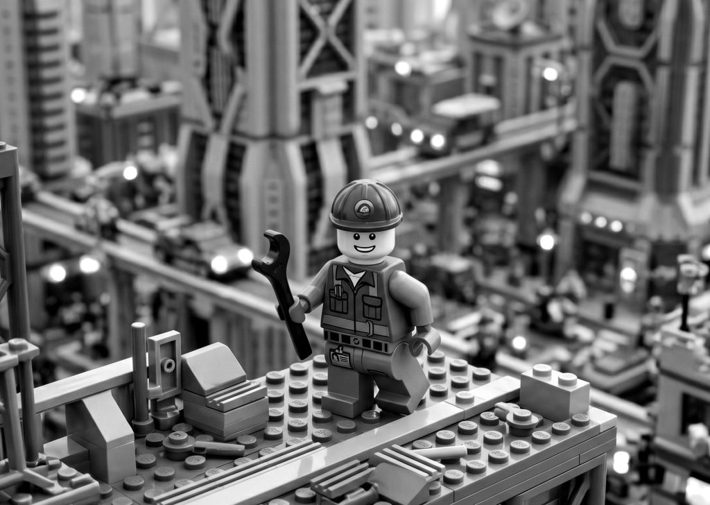 Black and white Lego construction worker holding a wrench over a detailed Lego city skyline, symbolizing ongoing technical support and mobile app maintenance.
