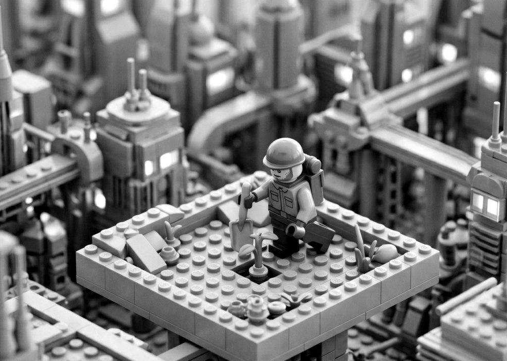 Black and white Lego minifigure planting a small sprout in a futuristic industrial cityscape, symbolizing the growth, foundation-building, and positive impact driven by nonprofit app development.