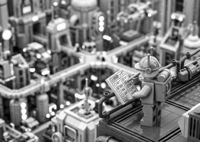 Black and white photo of a LEGO worker overlooking a complex, futuristic city while completing a checklist, representing the intricate planning steps of how to launch an app.